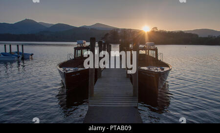 In Keswick, England, Großbritannien - 18 April 2009: der Sonne über den Derwent Fells Berge hinter Derwent Water Lake, wo ein paar Fähren günstig sind Stockfoto