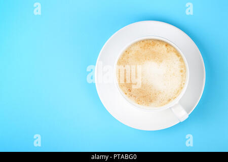 Schließen Sie eine volle weiße Tasse cremiger Latte Cappuccino und Untertasse über pastell-blaue Papier Hintergrund, erhöhte Ansicht von oben, direkt über Stockfoto
