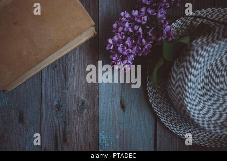 Zweig der Flieder, der Hut und Buch auf einem Holztisch Stockfoto