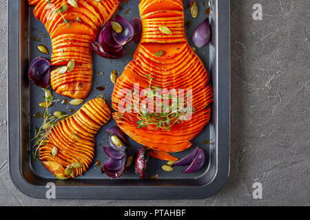 In dünne Scheiben geschnitten ganze Kürbisse gebacken mit roten Zwiebeln, frischem Thymian und Gewürze auf einem Backblech auf einen konkreten Hintergrund, Ansicht von oben, flach, Makro Stockfoto