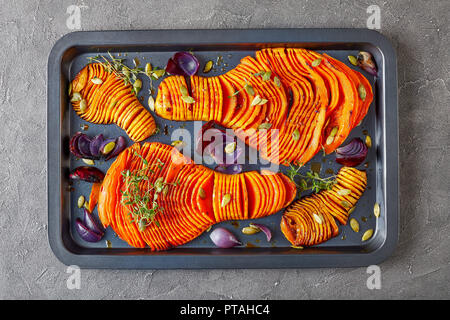 Dünn geschnittenen ganzen Kürbis gebacken mit roten Zwiebeln, frischem Thymian und Gewürze auf einem Backblech auf einen konkreten Hintergrund, Ansicht von oben, flach, Makro Stockfoto