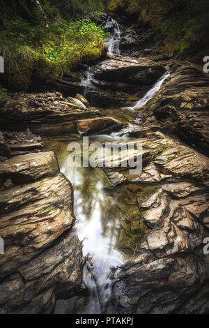 Kleinen Gebirgsbach Trøbekken im Wald in der Nähe von jonsvatnet See, mitten in Norwegen. Langzeitbelichtung Schuß auf dem Wasser und Felsen. Sommer. Stockfoto