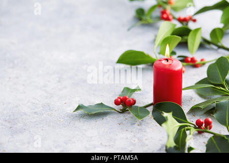 Weihnachtsschmuck, Kerzen mit immergrünen Dekorationen. Holly Blätter mit roten Beeren. Stockfoto