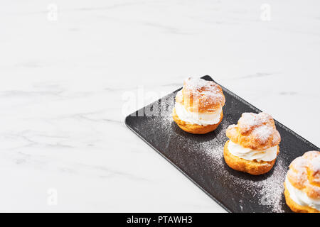 Blick von oben auf die leckere Softeis Kuchen mit Sahne und Puderzucker auf einer schwarzen Platte auf weißem Marmortisch. Selektiver Fokus, kopieren. Stockfoto