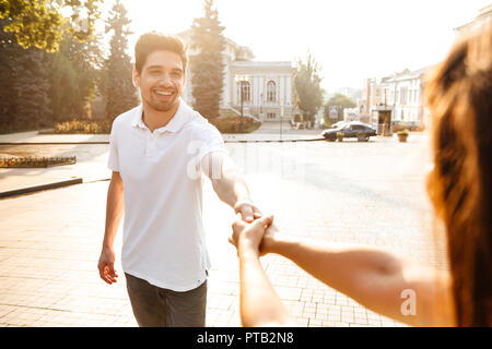 Bild der glückliche junge süße Paar Walking im Freien, während Sie die Hände der jeweils anderen. Stockfoto