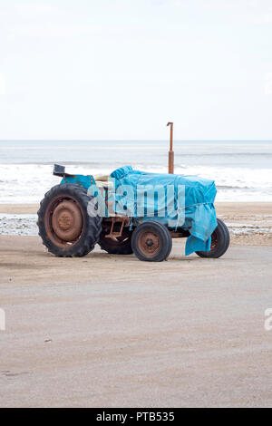 Einen alten Traktor für den Start der Fischerboote, in einer blauen Plane abgedeckt werden, auf einem Strand in Saltburn, North Yorkshire, UK geparkt Stockfoto