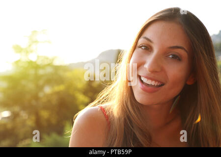 Lächelnde Frau mit perfekten Lächeln und weiße Zähne denken und suchen seitwärts im Park im Sommer. Sonnenlicht Flare. Kopieren Sie Platz. Stockfoto