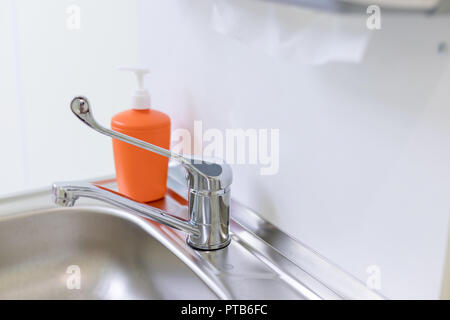 Orange Flasche für flüssige Seife in Zahnarzt, Arzt Büro. metall Waschbecken, flüssige Seife, Papier Handtücher. Gesundheit und Hygiene Konzept. Kopieren Sie Raum. Container mit flüssiger Seife. Der Ort für das Waschen der Hände. Konzept Hygiene und Reinheit der Hände. Stockfoto