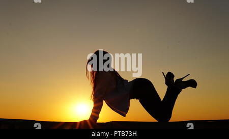 Junge Mädchen in Uniform sitzt auf der Kante des Dachs bei Sonnenuntergang Stockfoto