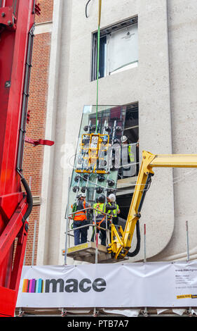 Bauunternehmer Mace Arbeiter auf Cherry Picker Hoist ein sorgfältig gerade neue große Glasscheibe in ein Gebäude in Mayfair, London, Großbritannien Stockfoto