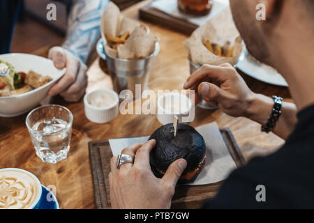 Freunde essen Burger und Pommes frites. Tabelle mit Nahrungsmitteln Blick von oben. Stockfoto