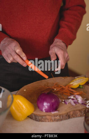 Ältere Menschen schneiden Möhre mit Messer in der Küche Stockfoto