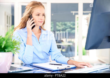 Portrait von schönen jungen Assistenten Geschäftsfrau, Anruf beim Sitzen am Schreibtisch und Arbeiten am Computer. Stockfoto