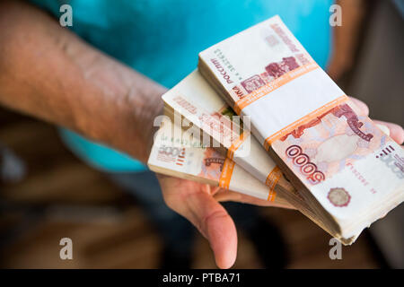 Mann Geld geben, Russische Rubel Banknoten, über seinen Schreibtisch in einem dunklen Büro - Bestechung und Korruption Konzept. russische Rubel Banknoten. Finanzielle Thema. Stapel von Banknoten in die Hand eines Mannes Stockfoto