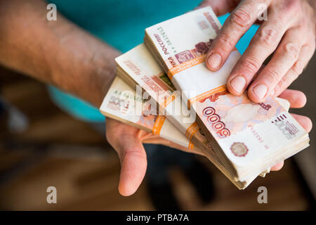 Mann Geld geben, Russische Rubel Banknoten, über seinen Schreibtisch in einem dunklen Büro - Bestechung und Korruption Konzept. russische Rubel Banknoten. Finanzielle Thema. Stapel von Banknoten in die Hand eines Mannes Stockfoto