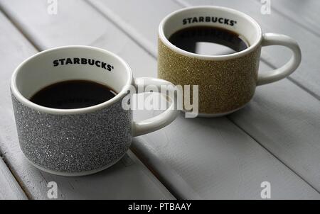 Zwei Starbucks Espresso Tassen mit einem glitzernden Thema Weihnachten mit Espresso auf einem grauen Lattenrost Tabelle verorten. Stockfoto
