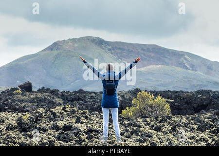 Rückansicht der jungen Frau mit Händen genießen einzigartige vulkanische Landschaften der Nationalpark Timanfaya auf Lanzarote im Winter auf den Kanarischen Inseln Stockfoto