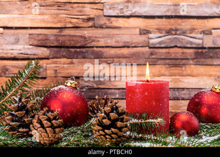 Weihnachtsdekoration mit Kerze, Christbaum Kugeln, Tannenzweigen und Tannenzapfen im Schnee vor Holz Hintergrund Stockfoto