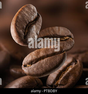 Geröstete Kaffeebohnen fallen auf Stapel. Dunkle Farben Stockfoto