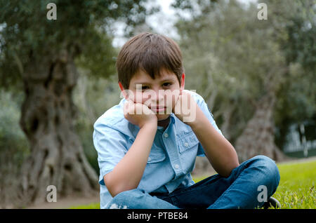 Toddler Boy mit lustigen Gesicht traurig oder gelangweilt. Er allein im Park sitzen auf Herbst Tag Stockfoto