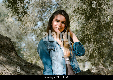 Schöne langhaarige Teenager Frau mit braunen Haaren lehnte sich an einen Baum im Park Stockfoto