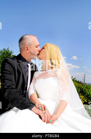 Hochzeit Konzept. Die happy stattliche Hochzeit paar Sitzen und Küssen. Der Bräutigam und Braut in Liebe umarmen. Im Hintergrund ist schön natürlich. Stockfoto