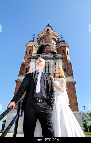 Hochzeit Konzept. Eine schöne Hochzeit paar steht auf der Treppe vor der schönen alten Kirche. Nette Leute für die Kamera posieren. Stockfoto