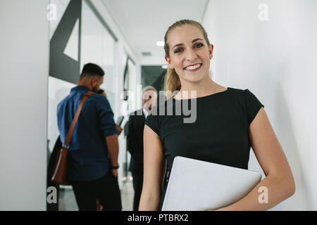 Porträt der glückliche junge Frau mit Laptop und lächelnd mit Ihrem Team besprechen im Hintergrund bei Büro Flur. Happy Geschäftsfrau im Amt Adr Stockfoto