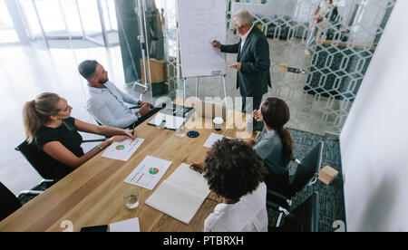 Reifen Geschäftsmann seine Ideen präsentieren auf dem Whiteboard zu Kollegen. Senior Manager eine Präsentation halten zu seiner Mannschaft im Konferenzraum bei Offi sitzen Stockfoto