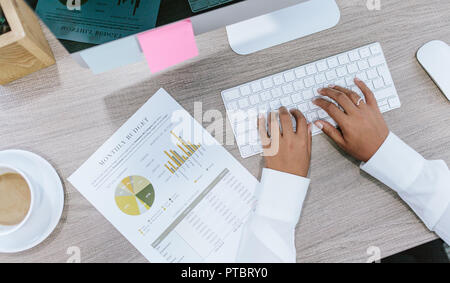 Draufsicht der weiblichen Hände, die auf der Tastatur am Schreibtisch tippen, mit statistischem Bericht. Geschäftsfrau an ihrem Arbeitsplatz. Stockfoto