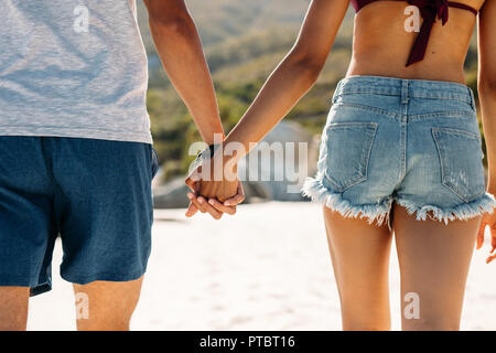 Ansicht der Rückseite ein Paar zusammen halten sich an den Händen. Romantisches Paar genießen am Strand an einem sonnigen Tag. Stockfoto