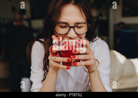 In der Nähe der weiblichen in Brillen Holding eine Kaffeetasse. Frau riechen den Duft von Kaffee im Cafe mit geschlossenen Augen. Stockfoto