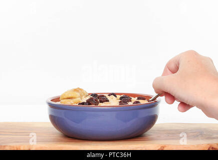 Seitenansicht Schüssel Haferbrei mit Hand utensil auf Holz- Platine mit weißem Hintergrund. Stockfoto
