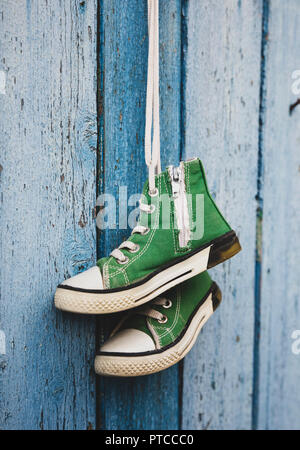 Paare der grünen alten Textil Kinder sneakers hängen an einer Schnur, blau schäbig Holz- Hintergrund Stockfoto