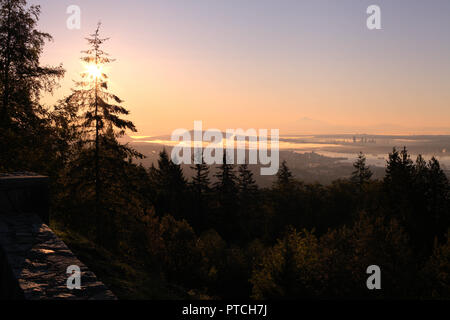 Die Stadt Vancouver, BC, Kanada, von Cypress Mountain Outlook gesehen, in der ersten Morgen Sonnenstrahlen, mit dunklen Koniferen und ein blau und rosa Himmel Stockfoto