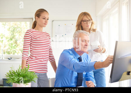 Kollegen sprechen während der Arbeit am neuen Finanzbericht. Senior Financial Advisor sitzen vor dem Computer und etwas zu ihr angezeigt Stockfoto