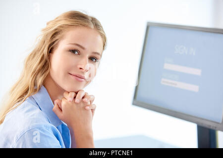 Close-up Portrait von schönen jungen Geschäftsfrau, die an der Kamera ein Lächeln, während Sitzen vor dem Computer. Stockfoto