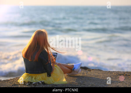 Rote Haare Mädchen ist Artist ist skizzieren. Sie sitzt am Kai von Meer in Abend und Zeichnung in einem Skizzenbuch Stockfoto