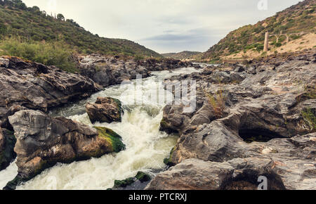 Stromschnellen des Flusses mit Rock mit grünen und gelben Moss mit bewölktem Himmel im Hintergrund Stockfoto