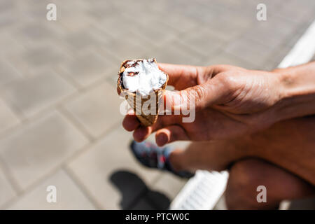 Mann hält eine Hälfte weiß Vanille Eis gelato Kegel auf italienische Straße in der Stadt während der heißen sonnigen Sommer Tag gegessen Stockfoto