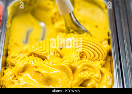 Makro Nahaufnahme von Mango Geschmack gelb orange gelato Eis mit Swirl Schaufel auf Anzeige im Cafe Shop in Italien, Italienisch Stockfoto