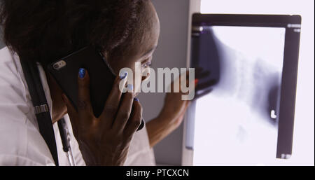 Senior afrikanische Arzt x-ray diskutieren mit Kollegen über Mobiltelefon Stockfoto