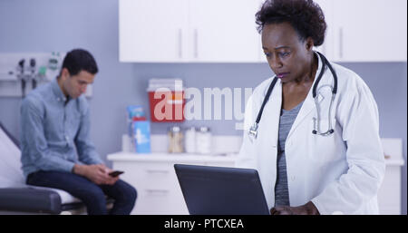 Portrait von Arzt mit tragbaren Computer ein, der den Noten der jungen männlichen Patienten aufnehmen Stockfoto
