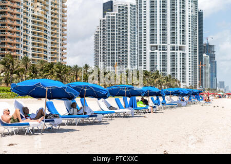 Sunny Isles Beach, USA - Mai 4, 2018: Viele ältere Menschen entspannen unter Sonnenschirmen auf Liegestühlen, Liegen am Strand an der Küste, Küste, Ufer ich Stockfoto