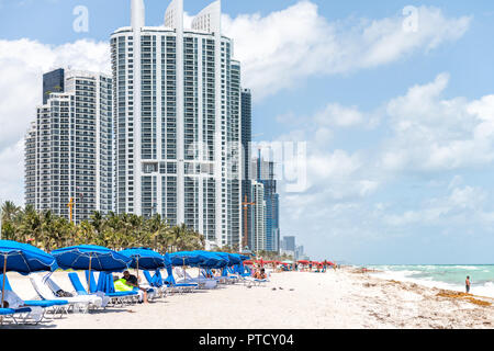 Sunny Isles Beach, USA - Mai 4, 2018: die Menschen entspannen unter Sonnenschirmen auf Liegestühlen, Liegen am Strand an der Küste, Küste, Ufer in Florida wi Stockfoto