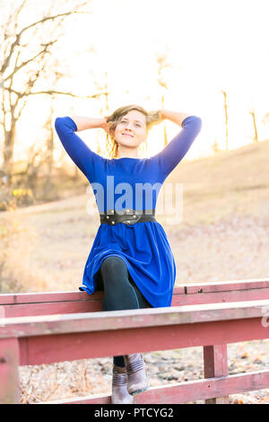 Junge Frau in der Natur saß oben auf der Holz- rot lackiert Brücke über den Bach, Fluss bei Sonnenuntergang, Sonnenaufgang im Herbst, Winter, Hintergrundbeleuchtung, Haar, mit Hintergrundbeleuchtung Stockfoto