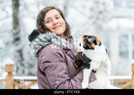 Nahaufnahme der junge Frau mit wütend, erschrocken miauen Calico Katze draußen, im Freien auf Haus Deck, im Park im Schnee, Schnee Wetter während Schneesturm, st Stockfoto