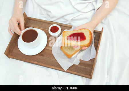 Das Mädchen ist Frühstück im Bett, mit Holz- Fach mit Toast mit Marmelade und Kakao Stockfoto