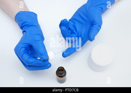 Die Hände des Arztes in Handschuhe mit einer Flasche und Rückgang der Mittel auf einen Finger aus einer Pipette auf weißem Hintergrund Stockfoto