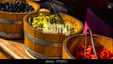 Grüne pepperone, schwarze Oliven und geschnittene rote Paprika in großen holzbottichen. Stockfoto
